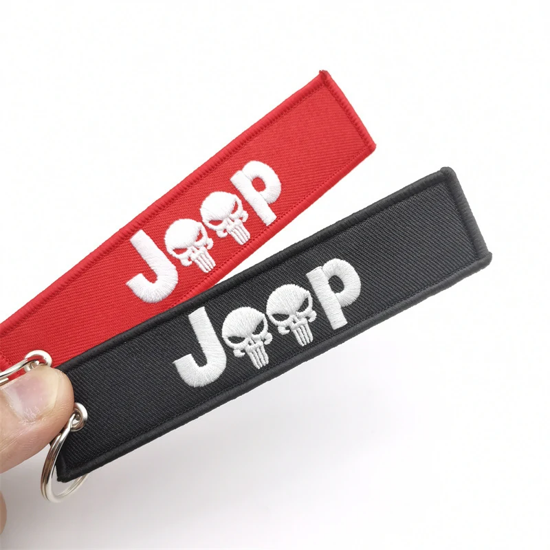 A hand holding red and black Jeep themed fabric keychain tags with metal rings.