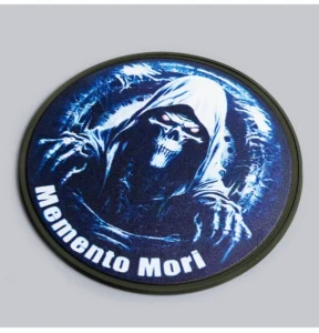 Round dark embroidered patch featuring a hooded figure and Memento Mori lettering.