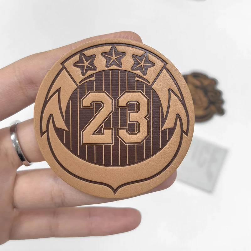 Hand holding a round tan number 23 logo patch to show scale and surface detail.