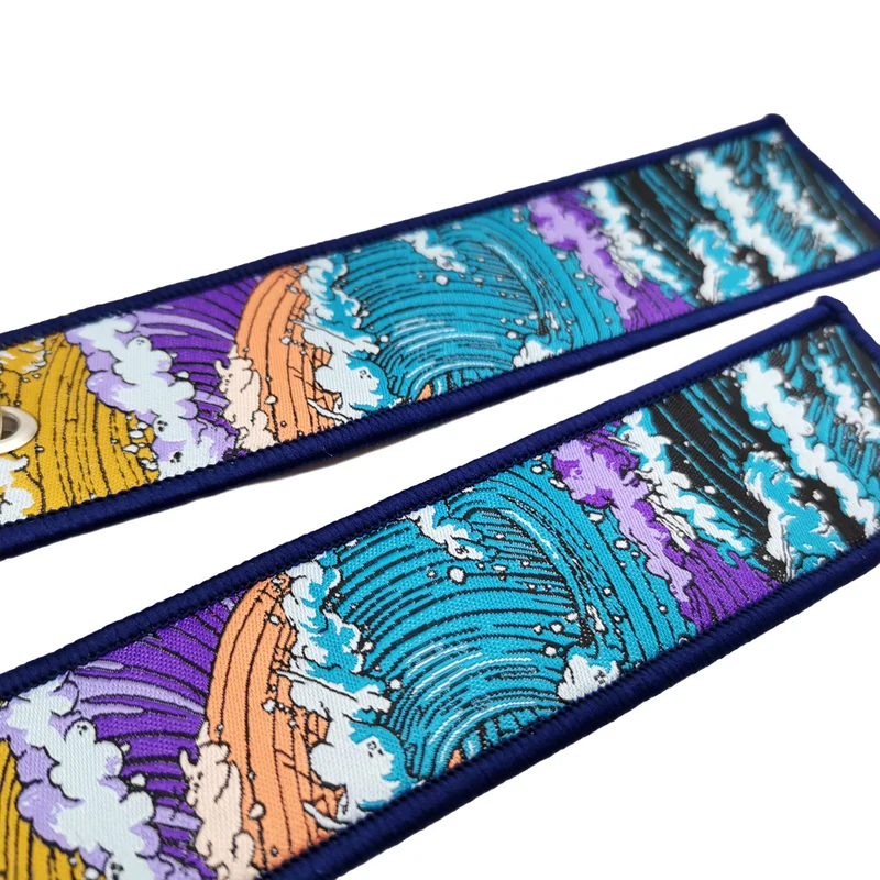 Two long fabric key tags featuring a multicolor illustrated wave pattern on white.