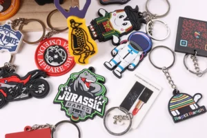 Collection of colorful soft PVC keychains with motorcycle, dinosaur, astronaut and logo designs.