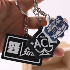 Hand holding several black and white custom soft PVC logo keychains with metal rings.