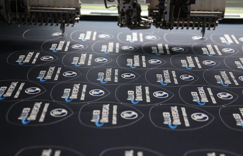 Multihead embroidery machine stitching rows of white logos on black fabric