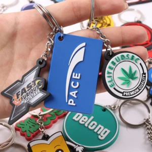 Hand holding blue PACE tag and circular green leaf logo soft PVC keychains.