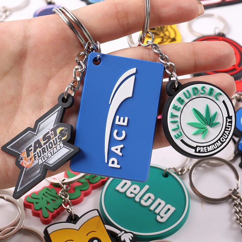 Hand holding blue PACE tag and circular green leaf logo soft PVC keychains.