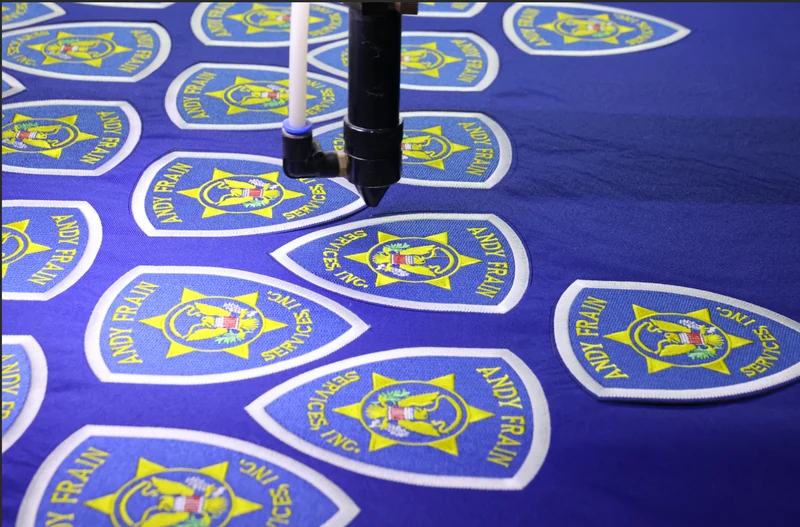 Machine cutting repeated blue and yellow emblem shapes from fabric sheet