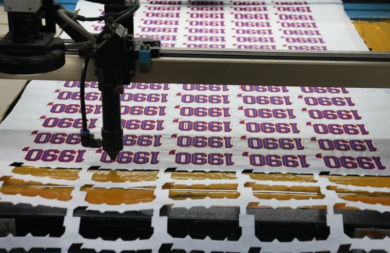 Cutting machine working on sheet of repeated 1980 number patch designs