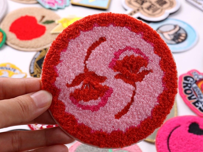 Round pink and red custom chenille patch with a textured stylized face design and raised border