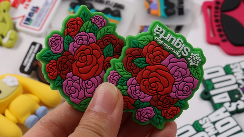 Hand holding two green PVC patches with raised red and pink rose designs