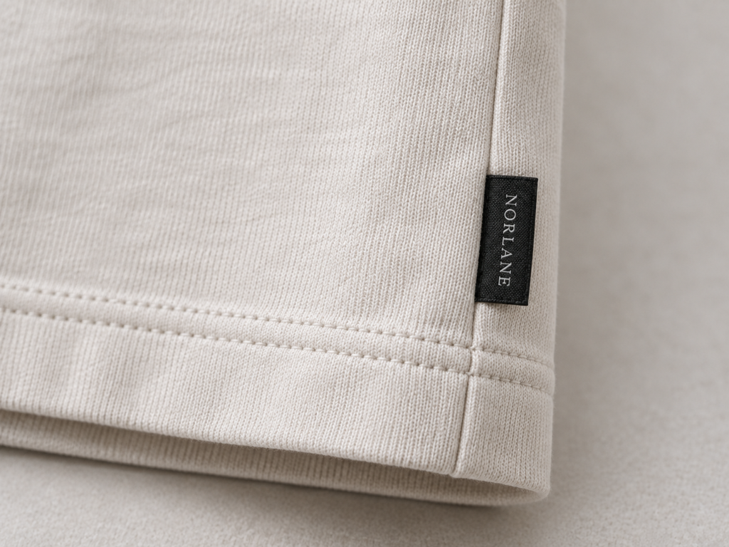 Small black folded NORIANE woven label sewn into the side seam of a cream garment
