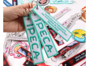 White and turquoise IPECA embroidered fabric keychains with logo lettering and metal rings