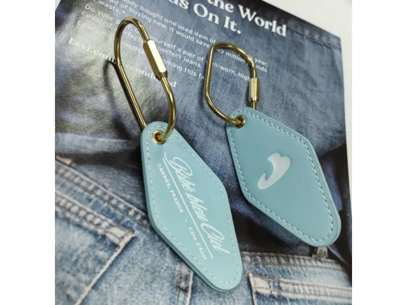 Two light blue custom PU leather keychains with printed logos and gold-tone carabiner clips