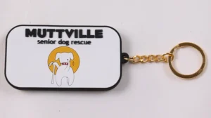 White rectangular PVC keychain with senior dog rescue logo and gold ring