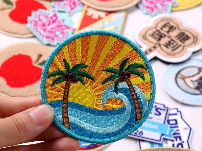 Round custom embroidered patch with palm trees, ocean waves, orange sunset and turquoise merrow border