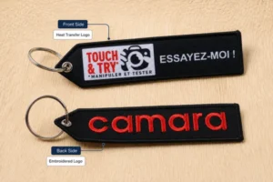 Two black fabric keychains with embroidery shown on their front and back