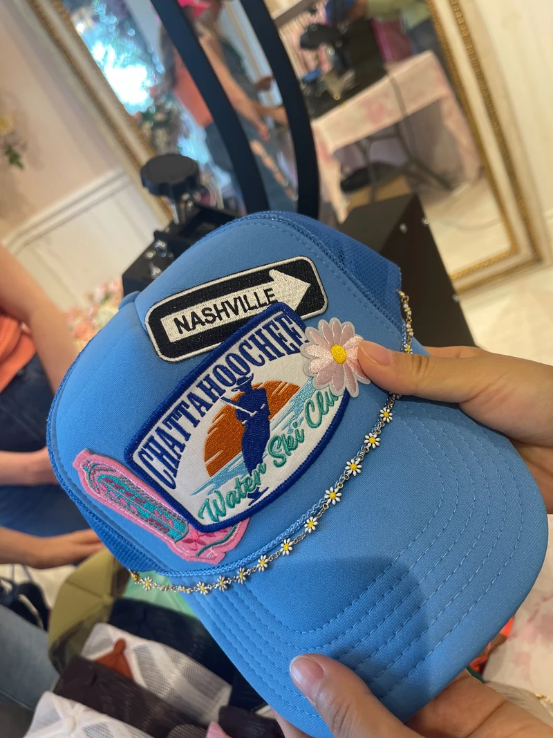 Hand holding a blue mesh cap with a colorful souvenir patch on the front.