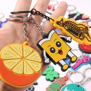 Hand holding orange slice and yellow cartoon figure PVC keychains by silver rings.