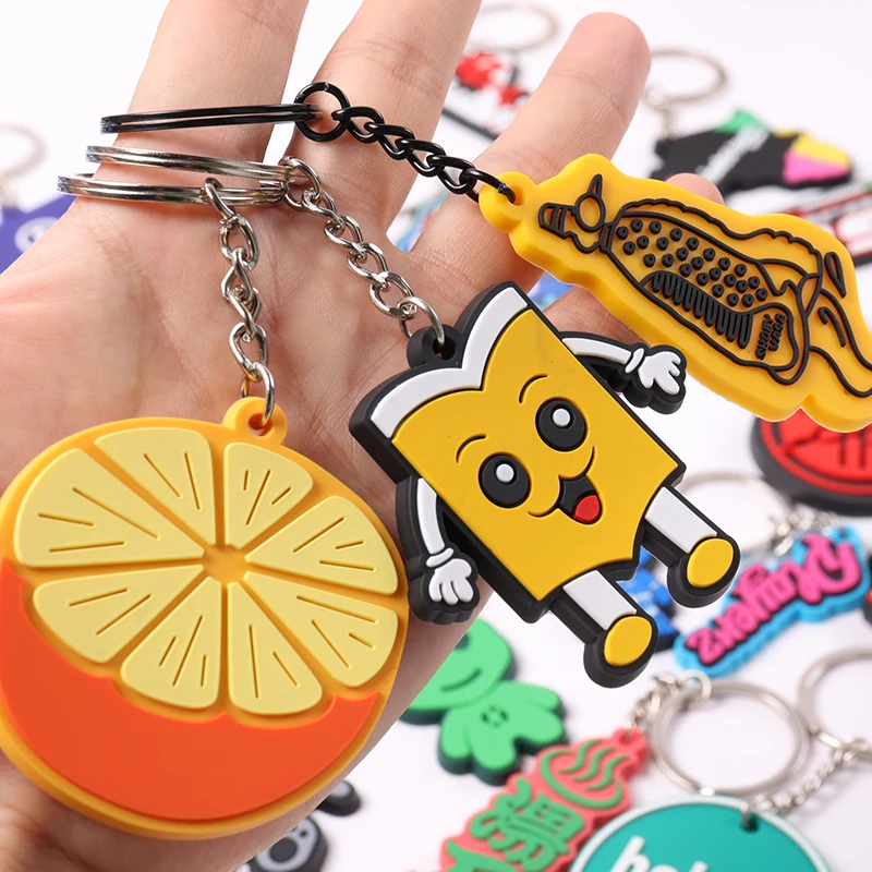 Hand holding orange slice and yellow cartoon figure PVC keychains by silver rings.