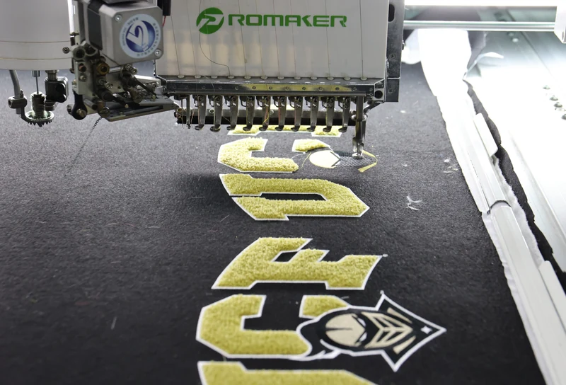Embroidery machine stitching yellow number and shield design on dark fabric