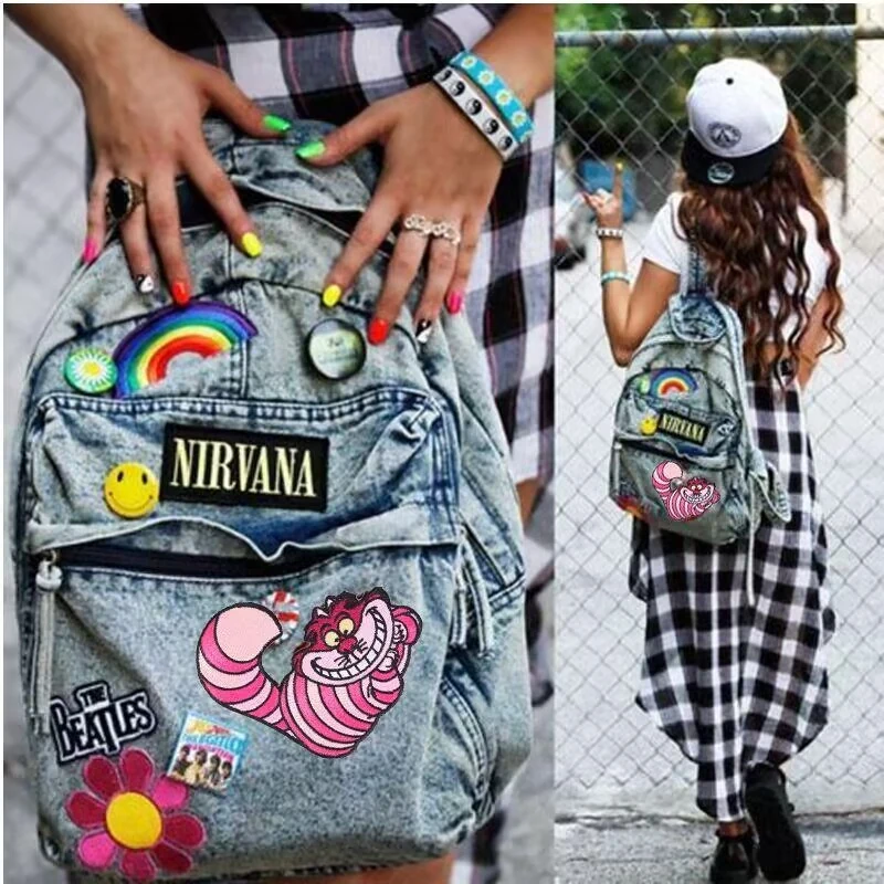 Denim backpack decorated with colorful music and cartoon patches in a street scene.