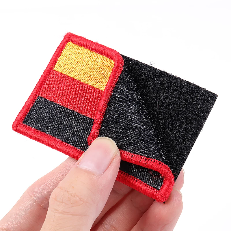 Hand holding a small red rectangular fabric patch with black hook and loop backing.