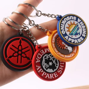 Hand holding several circular soft PVC keychains with black, blue, red and orange emblems.