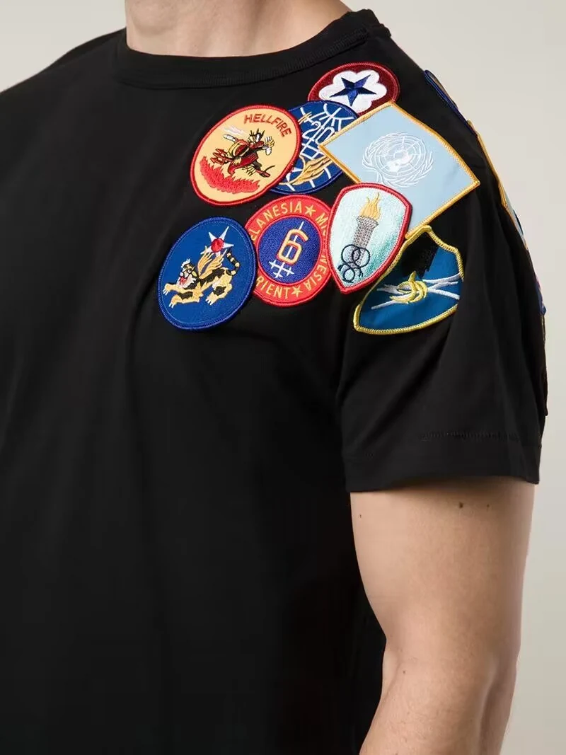 Black T-shirt decorated with several colorful round embroidered patches.