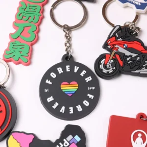 Black circular pride design PVC keychain beside a red motorcycle rubber keyring.