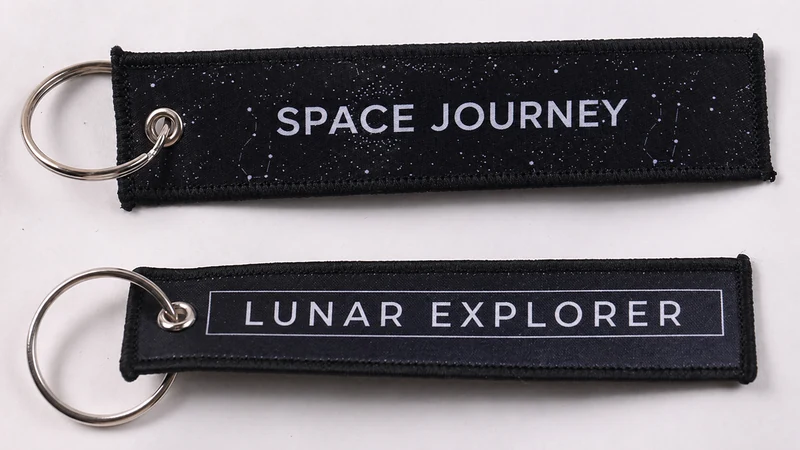 Two black fabric keychains marked Space Journey and Lunar Explorer
