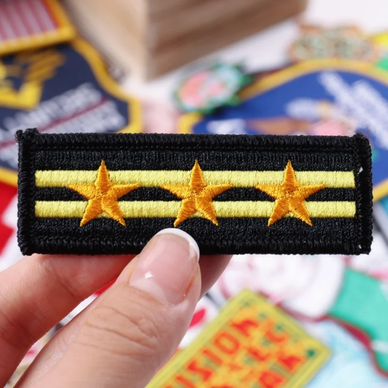 Black rectangular embroidered badge with three gold stars and two gold stripes