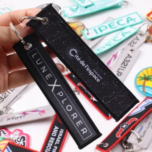 Two black fabric keychain tags with white Tune In More lettering