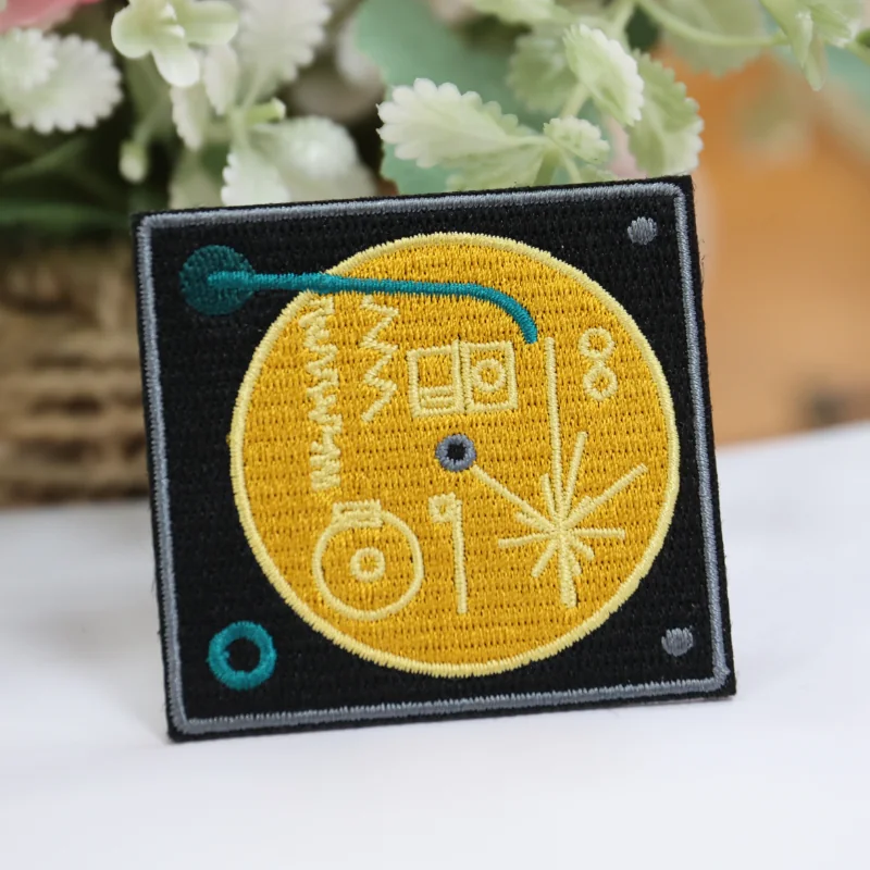 Black square embroidered patch with a yellow circular line art design