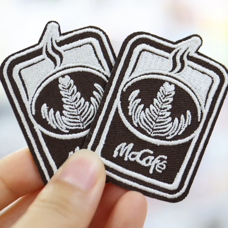 Two coffee-cup-shaped patches with white steam and latte-art embroidery and McCafe lettering on a brown base.